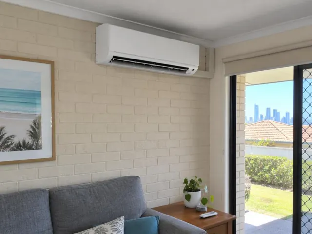 Clean split-system indoor unit mounted high on a painted brick living room wall in Broadbeach