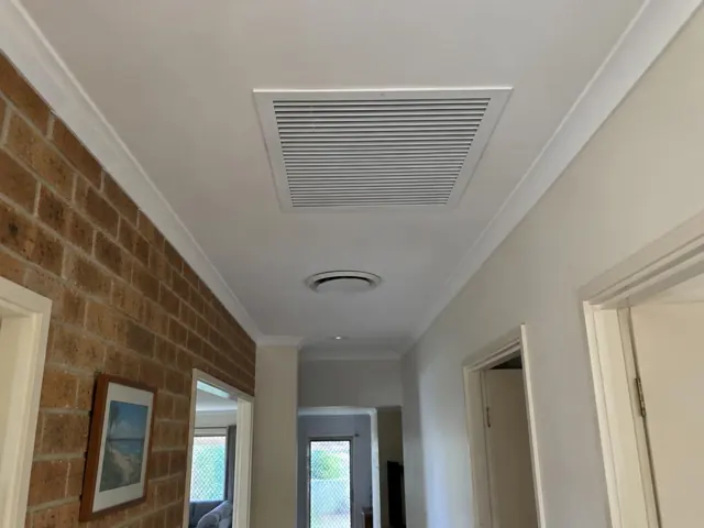 Hallway ceiling with a return-air grille and round vent above a brick feature wall in Mermaid Waters
