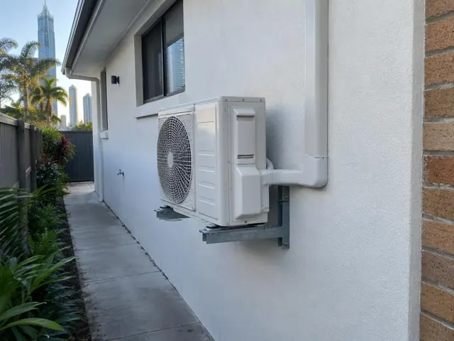 Wall-mounted outdoor air conditioner unit beside a narrow side path on a modern house in Surfers Paradise